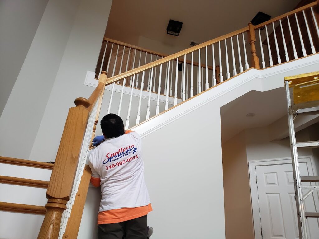 A person in a branded t-shirt paints a wooden staircase railing indoors. The setting is bright and orderly, conveying a sense of focus and care.